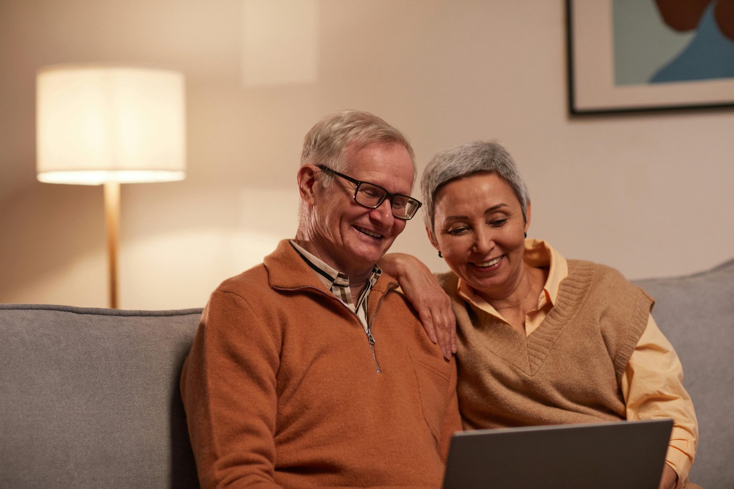 Smiling elderly couple sitting in a low lit room on a laptop